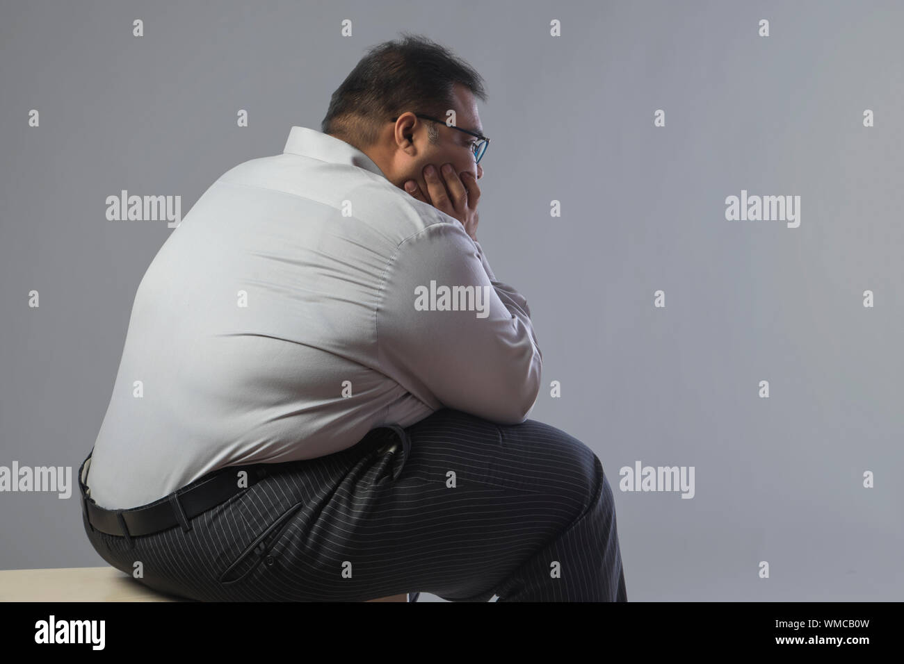 Side view of obese man sitting in sad mood with chin resting on hand Stock Photo