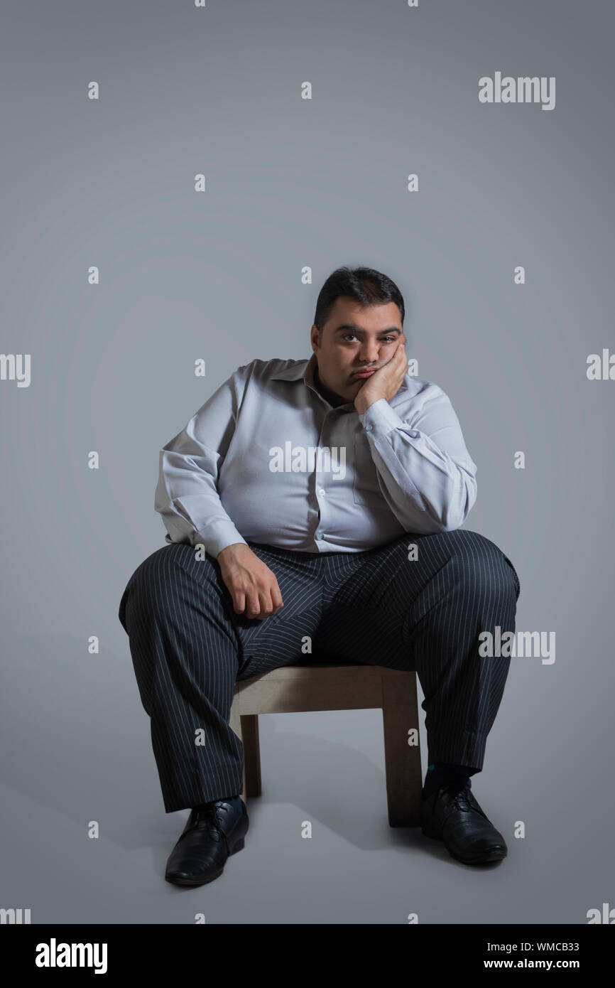 Overweight man sitting on chair in sad mood with chin resting on hand Stock Photo