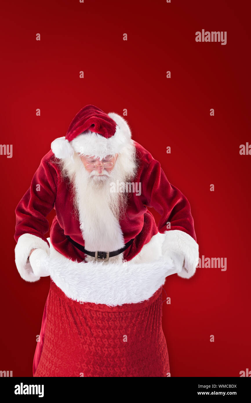 Santa looks in his bag against red background Stock Photo - Alamy