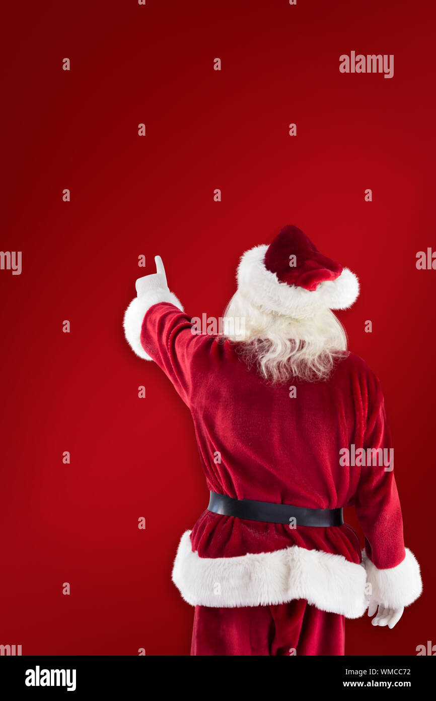 Santa Claus points at something against red background Stock Photo
