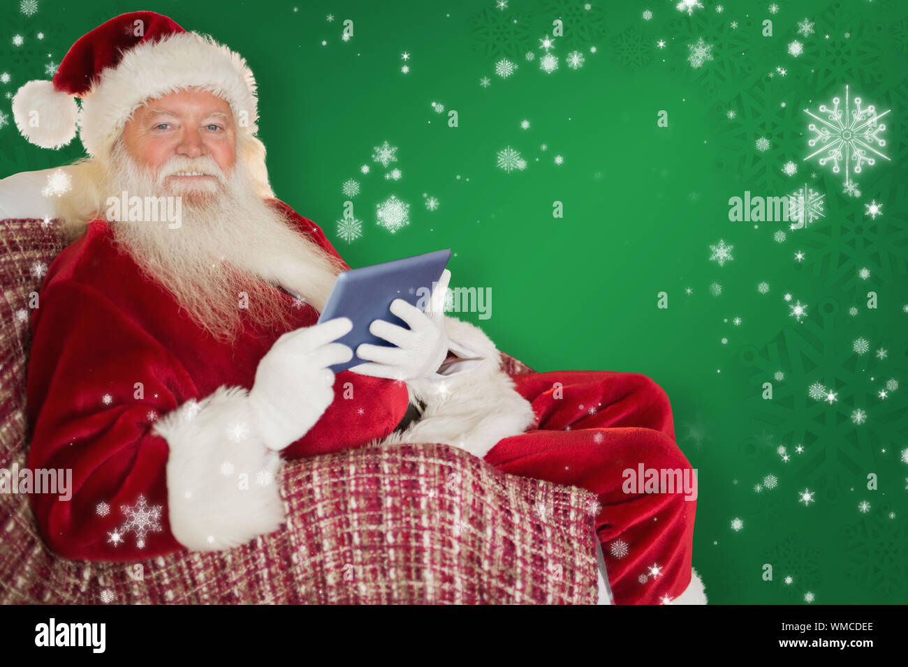 Smiling santa using tablet on the armchair against green snowflake ...