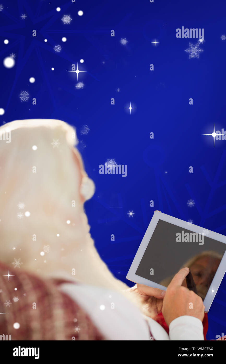 Rear view of santa using tablet on the armchair against blue snowflake ...