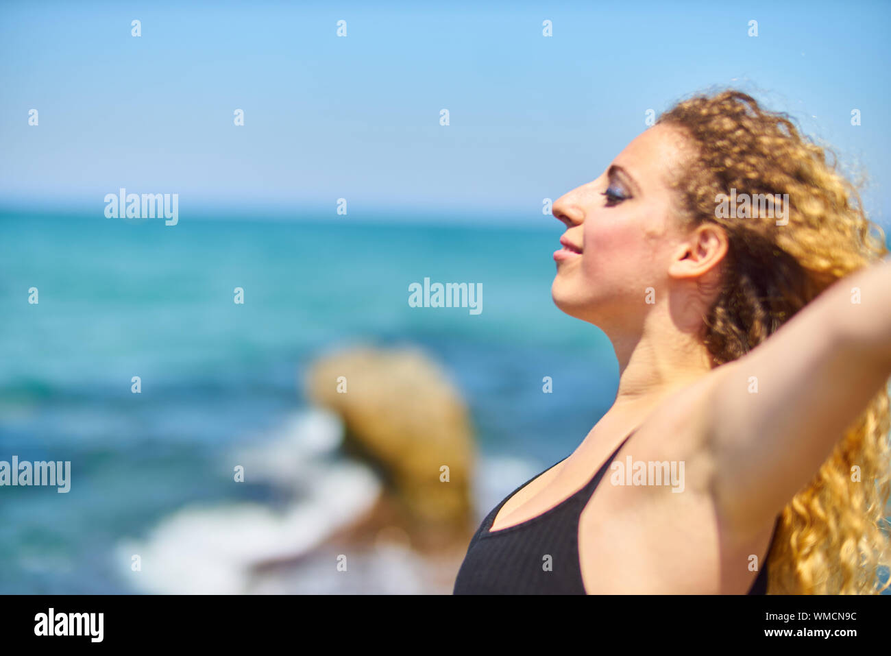 Young Woman With Blond Curly Hair At Beach Against Sky Stock Photo