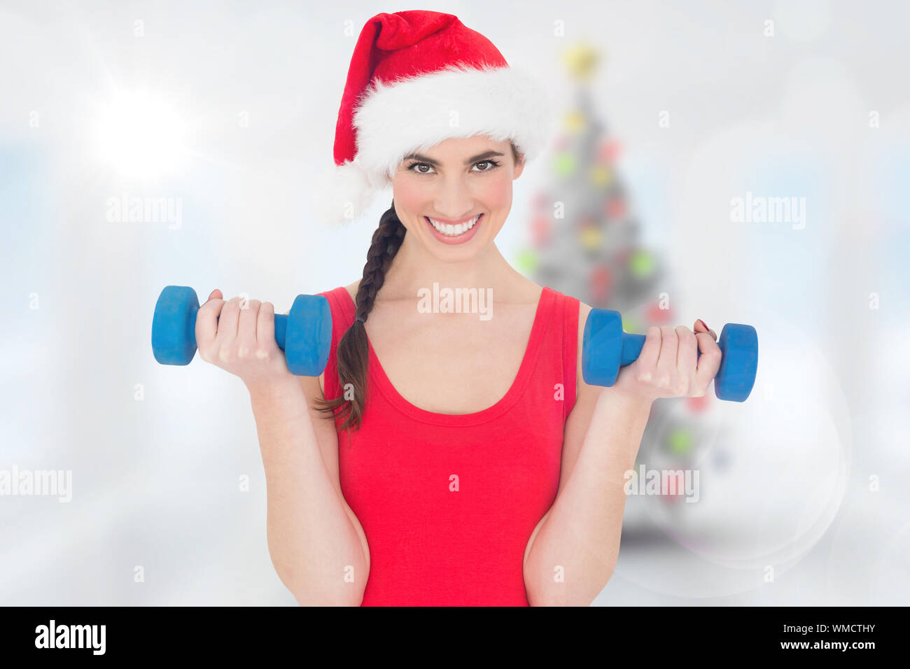 Festive fit brunette holding dumbbells against blurry christmas tree in room Stock Photo