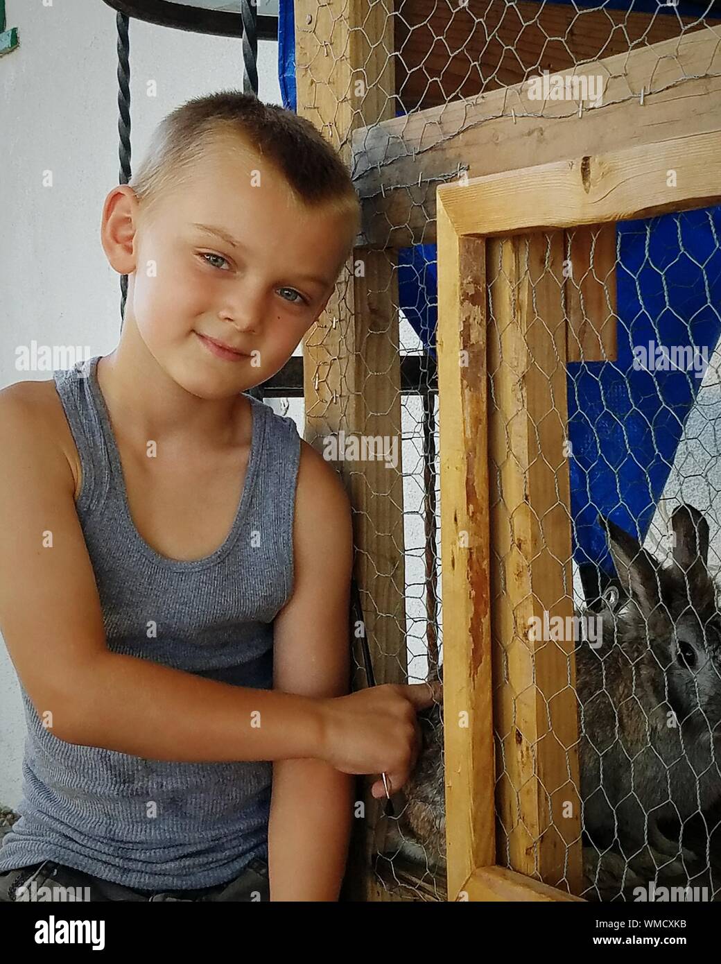Portrait Of Smiling Boy Standing By Rabbit Hutch Stock Photo