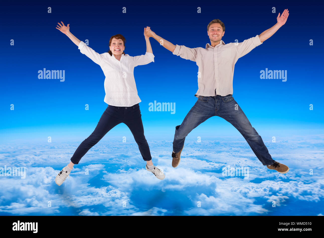 Couple jumping and holding hands against blue sky over clouds at high ...