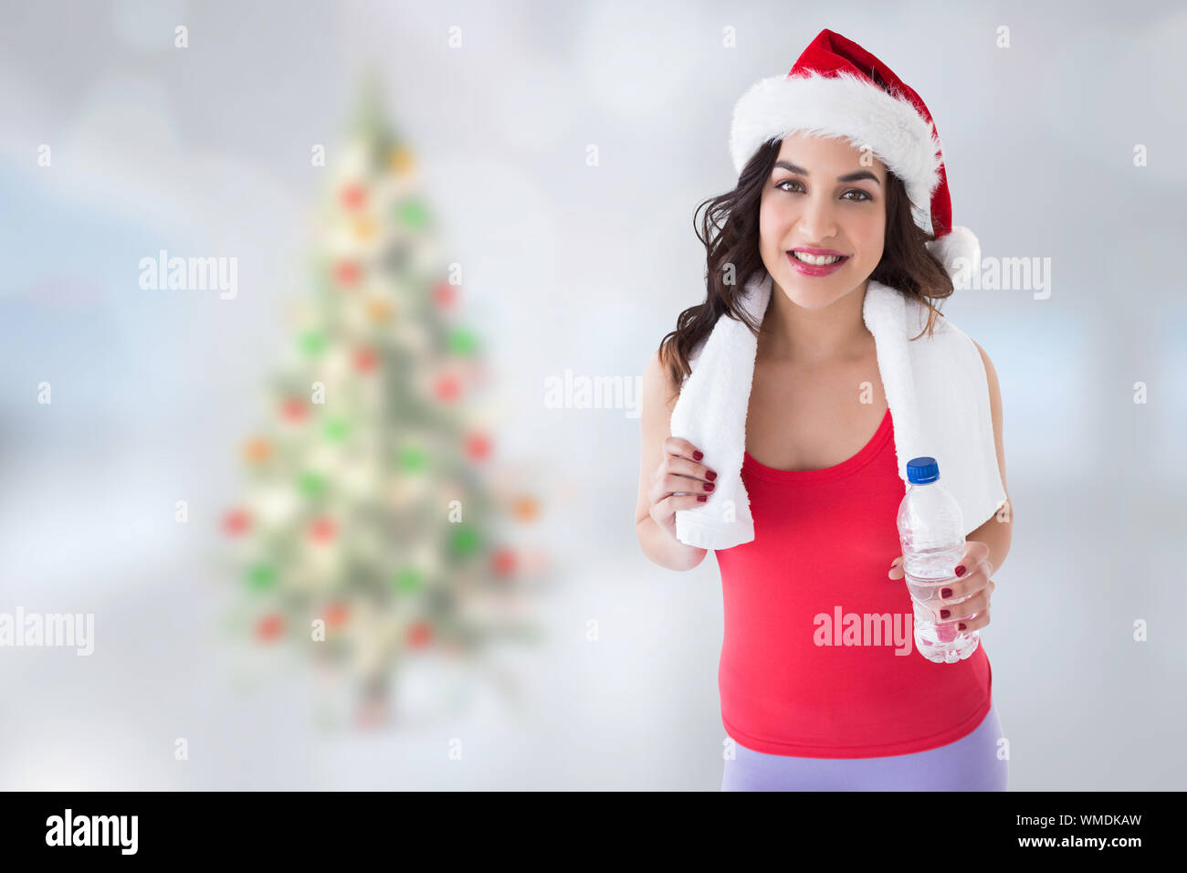 Festive fit brunette holding bottle against blurry christmas tree in room Stock Photo