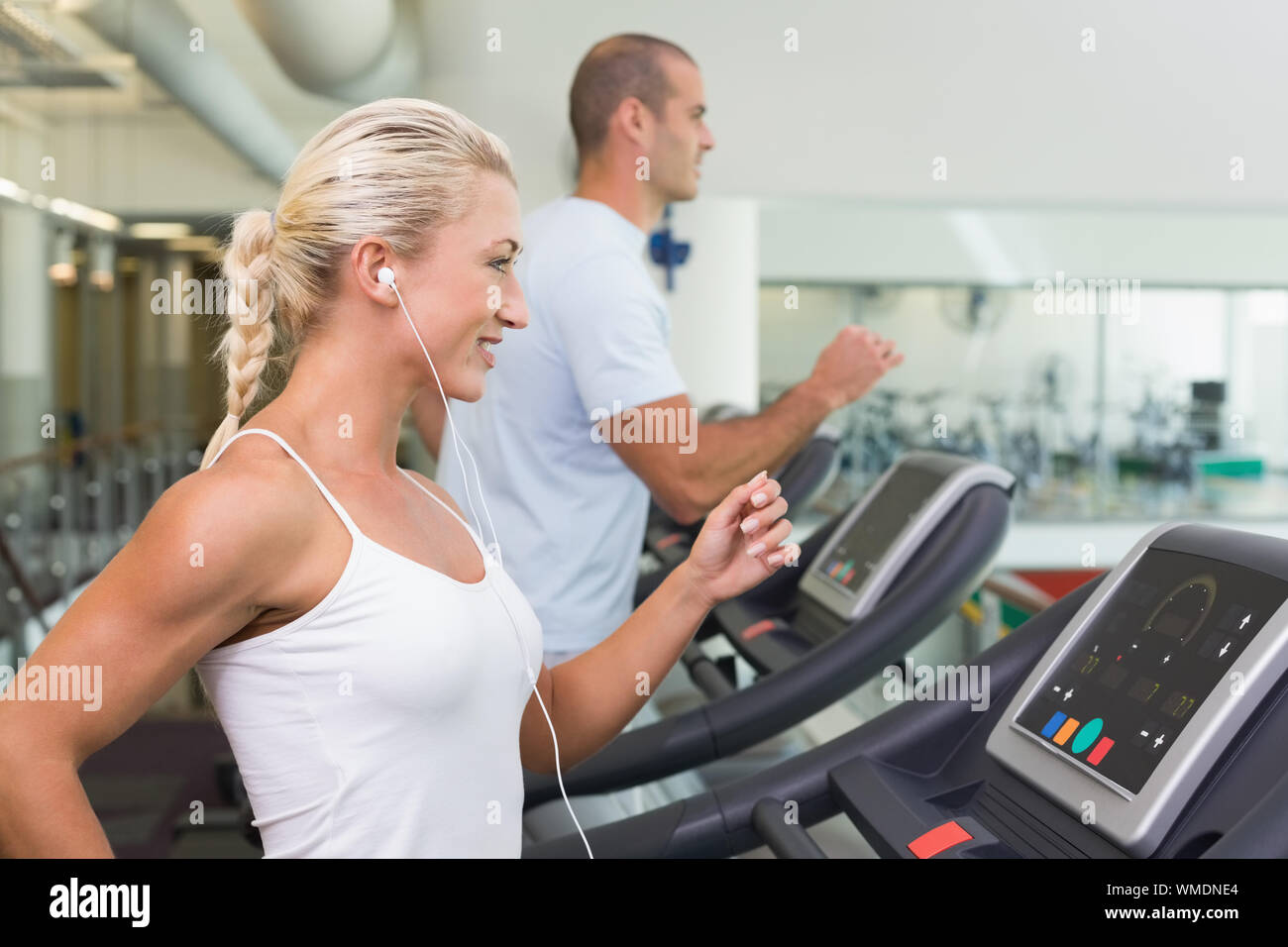 Side view of a fit young couple running on treadmills at the gym Stock ...