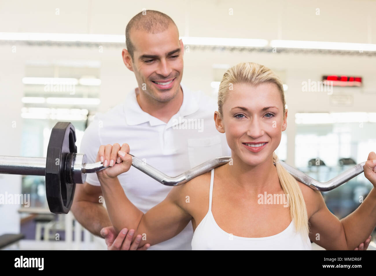 Personal male trainer helping young woman with lifting barbell in the ...