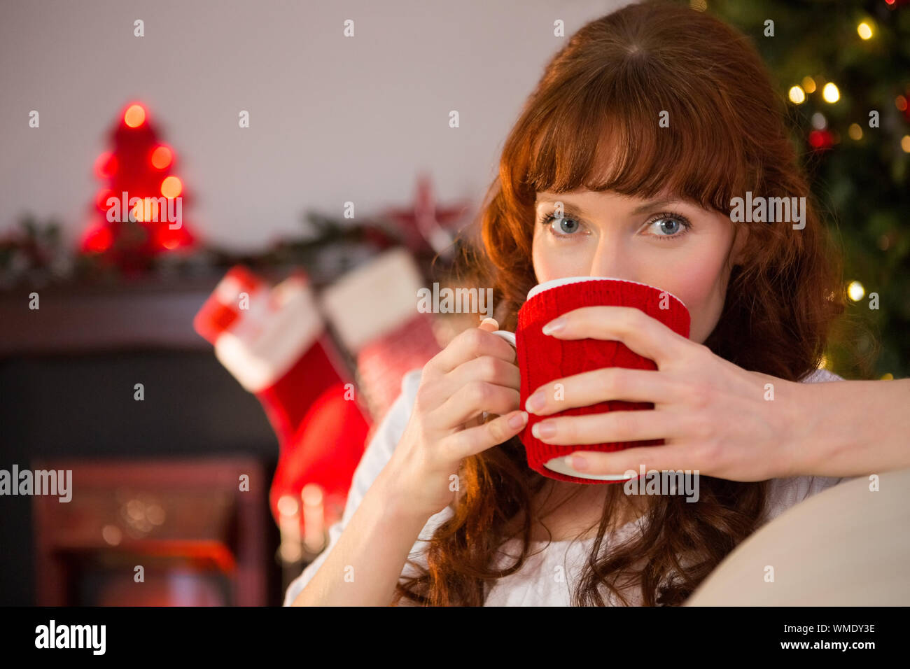 Pretty redhead sitting on couch drinking hot chocolate at christmas at christmas at home in the living room Stock Photo