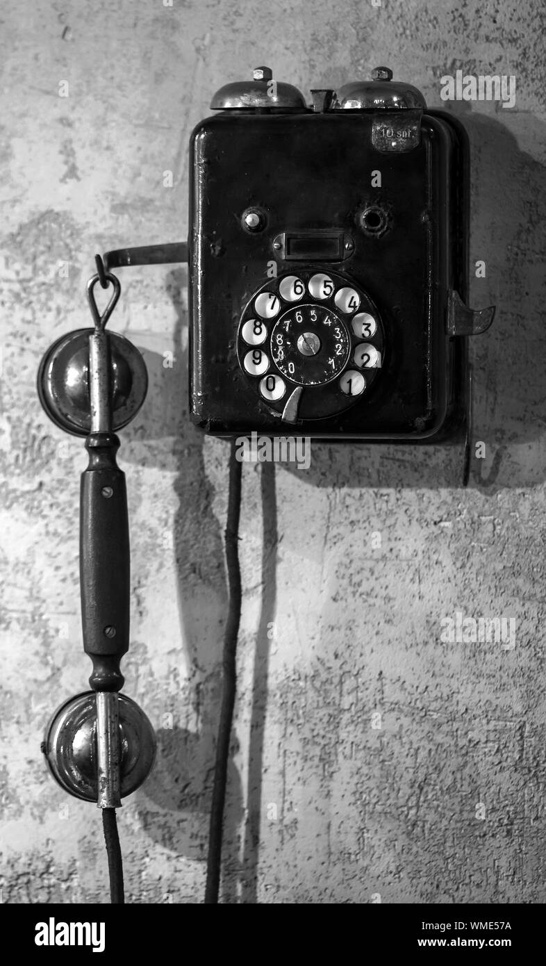 Vintage black phone hanging on old gray concrete wall. Black and white, retro style photo Stock Photo