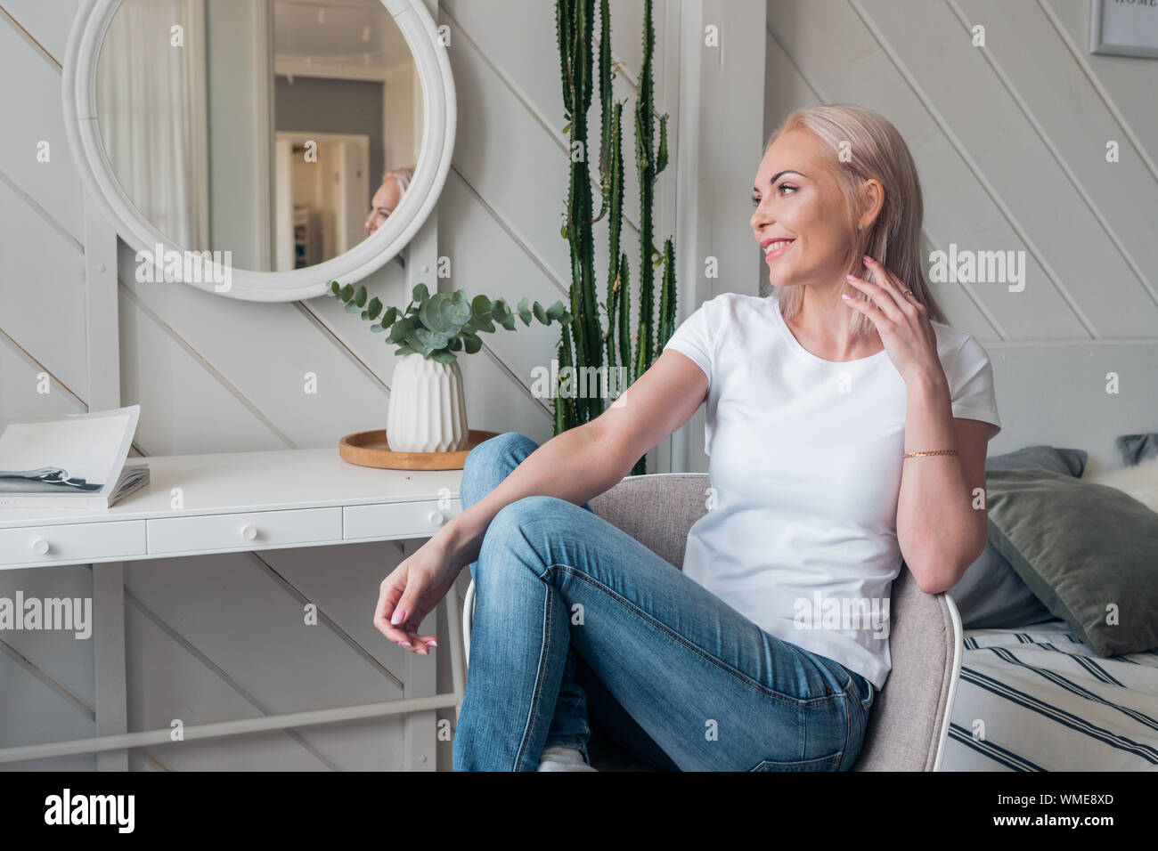 Beautiful blonde in casual clothes is sitting on a chair and dreaming Stock Photo