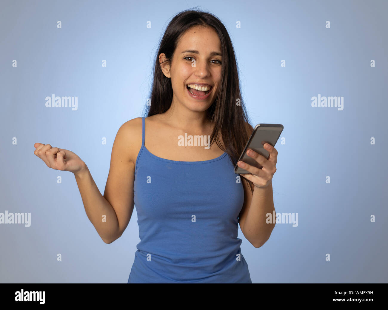 Young latin woman on mobile looking happily shocked at social media app dating site. Teenager girl having lots of followers and likes on online video Stock Photo