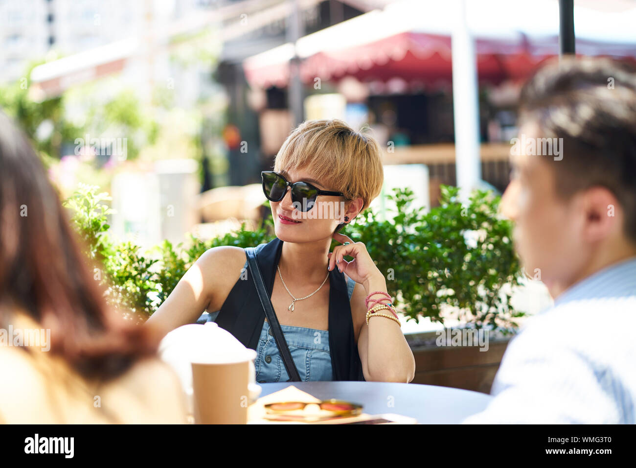 young asian woman smiling while talking to friends in outdoor coffee shop Stock Photo