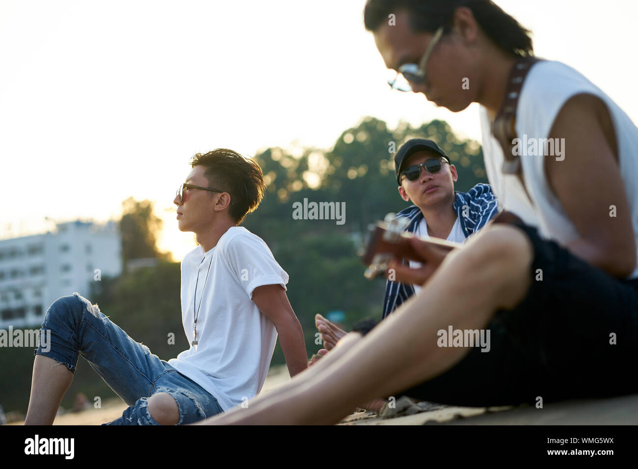 young asian adult men sitting on beach relaxing and playing guitar Stock Photo