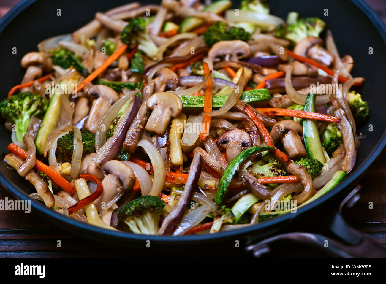 Sauted Chopped Vegetables in Juliana: Zucchini, Onions, Eggplant, Carrots, Mushrooms and Broccoli inside an skillet over a vintage wooden surface Stock Photo
