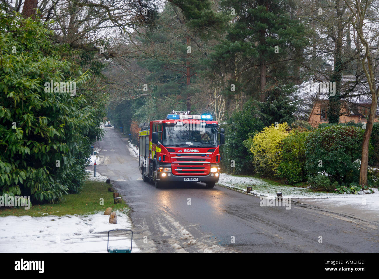 A red Scania P270 fire engine with flashing lights attends an emergency on a cold snowy morning in winter, Woking, Surrey, southeast England Stock Photo