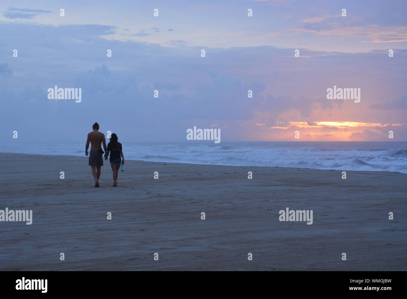 A couple walks down the beach on Ocracoke Island at sunrise on the North Carolina Outer Banks. Stock Photo