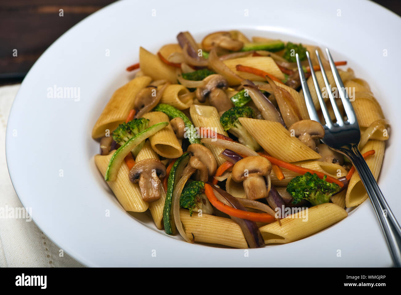 Hot dish of Penne Rigate noodles with Sauted Vegetables in Juliana: Zucchini, Onions, Eggplant, Carrots, Mushrooms and Broccoli in a white pasta plate Stock Photo