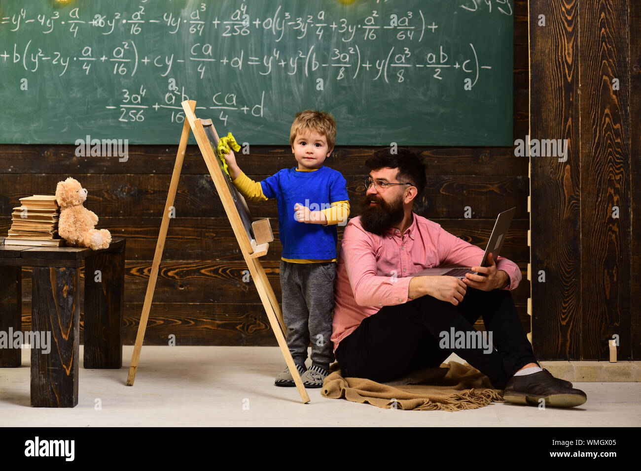 Teacher looking at kid wiping chalkboard. Smiling man in glasses