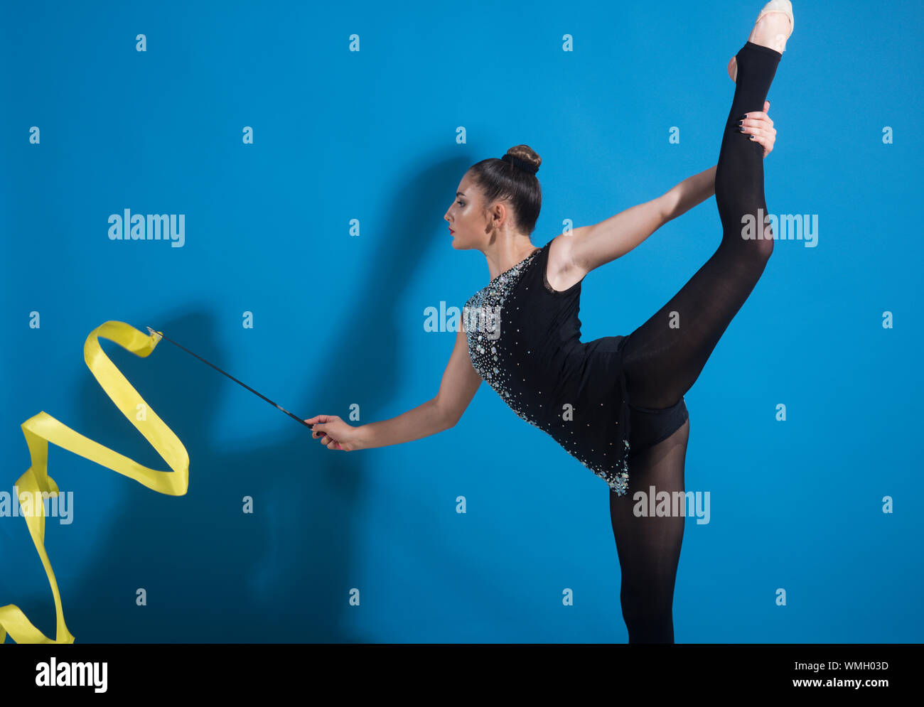 beautiful Caucasian girl gymnast with yellow ribbon in split. Stock Photo