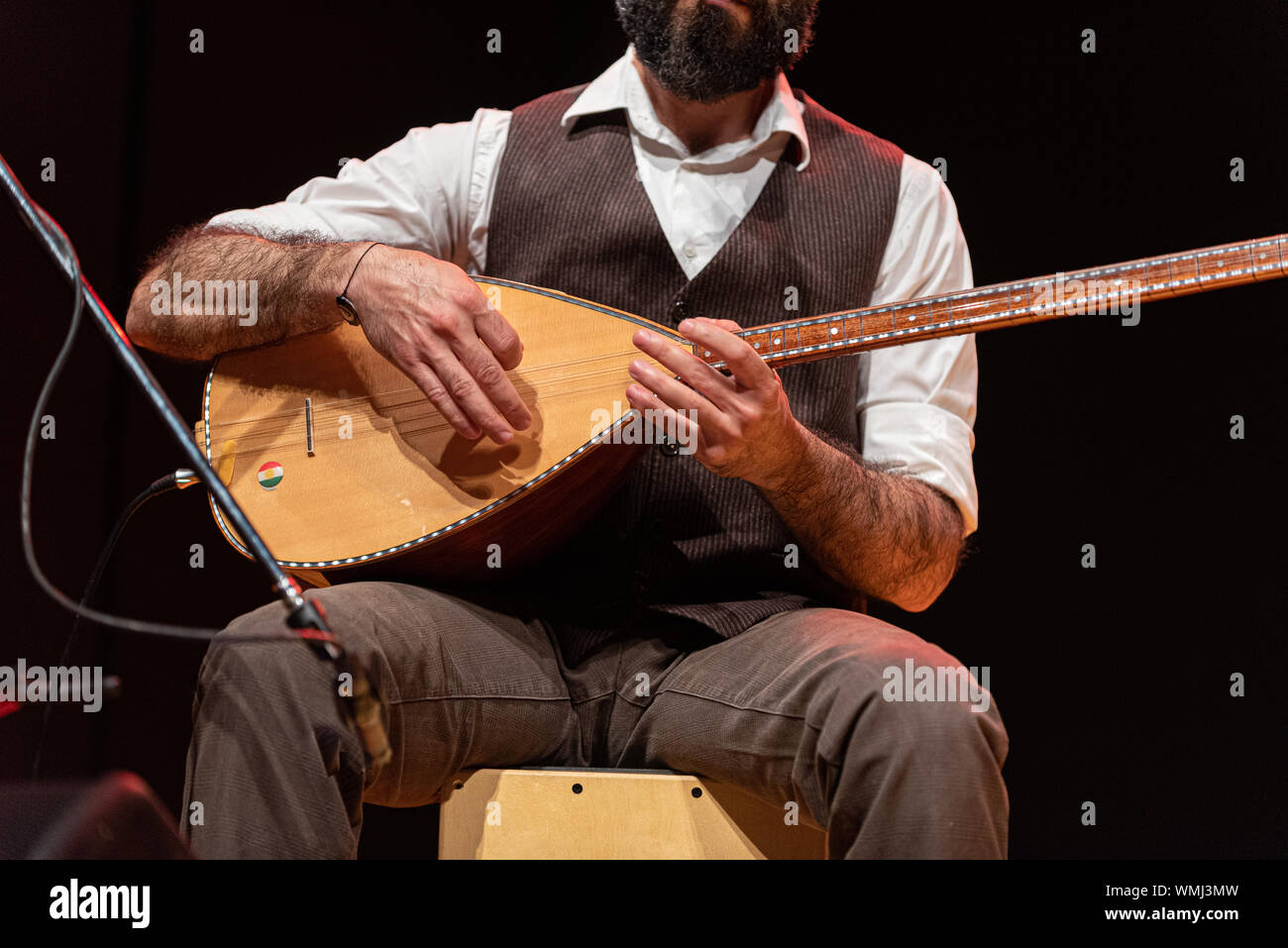 Good-looking man with a thick black beard, hands details of a musician playing a typical stringed instrument on stage, the tembur or saz Stock Photo