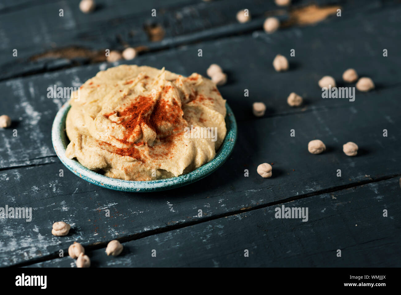 closeup of a green ceramic plate with homemade hummus seasoned with paprika, on a dark gray rustic wooden table Stock Photo