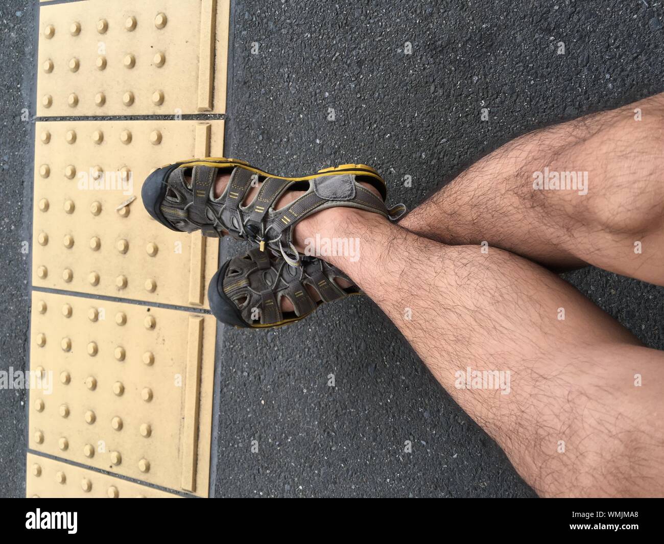 Low Section Of Man Sitting By Tactile Paving On Road Stock Photo
