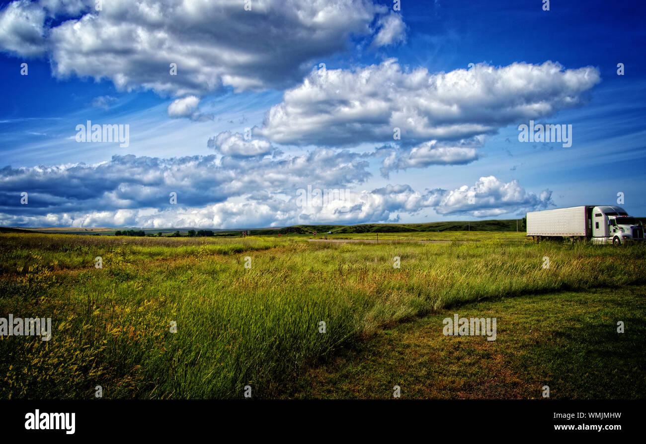 18 wheeler traveling through beautiful landscape with beautiful clouds, Stock Photo