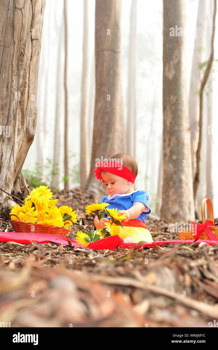 Baby Girl With Flower Basket Sitting At Forest Stock Photo