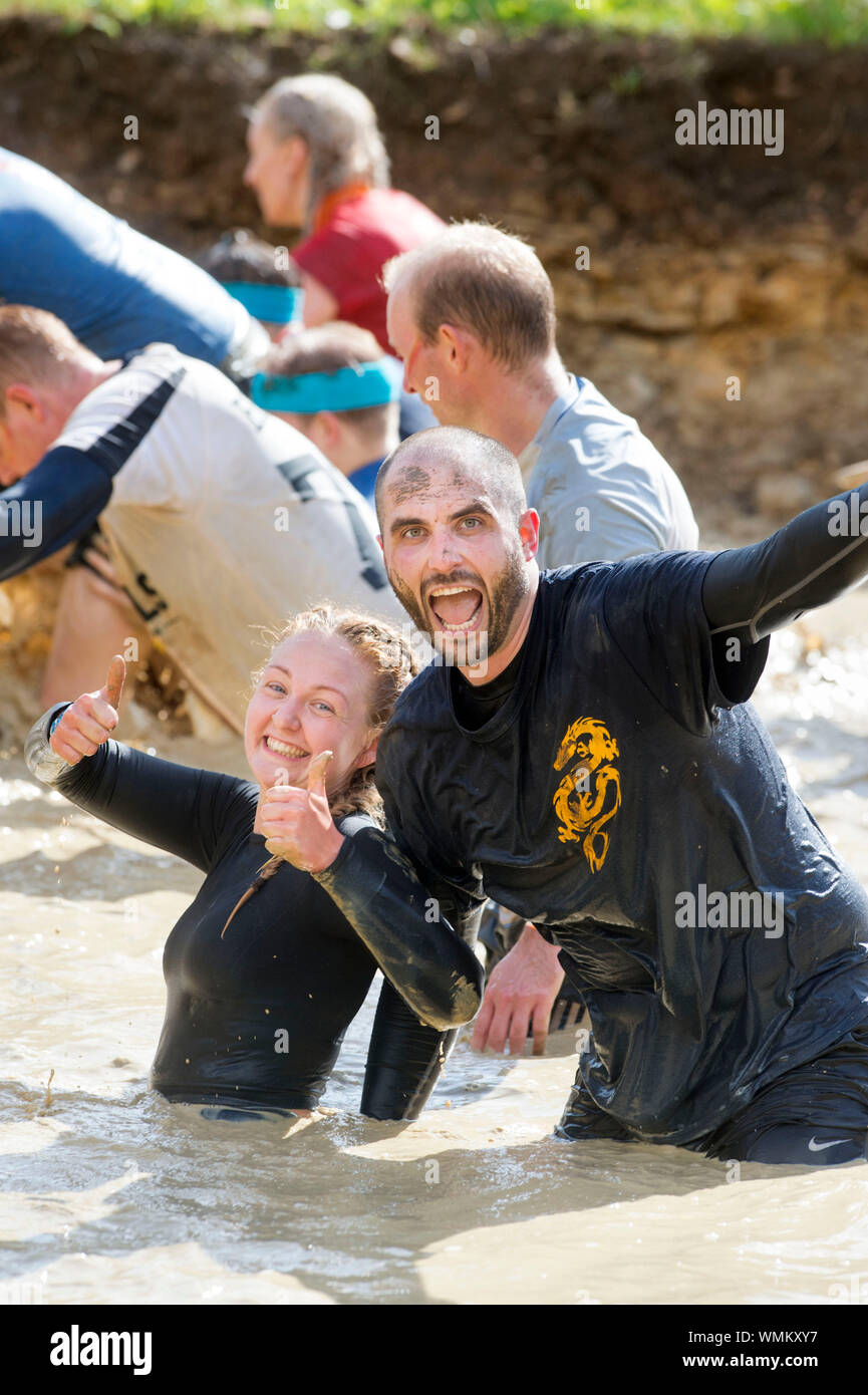 A couple negotiate the ‘Mud Mile’ obstacle at the Tough Mudder endurance event in Badminton Park, Gloucestershire UK Stock Photo