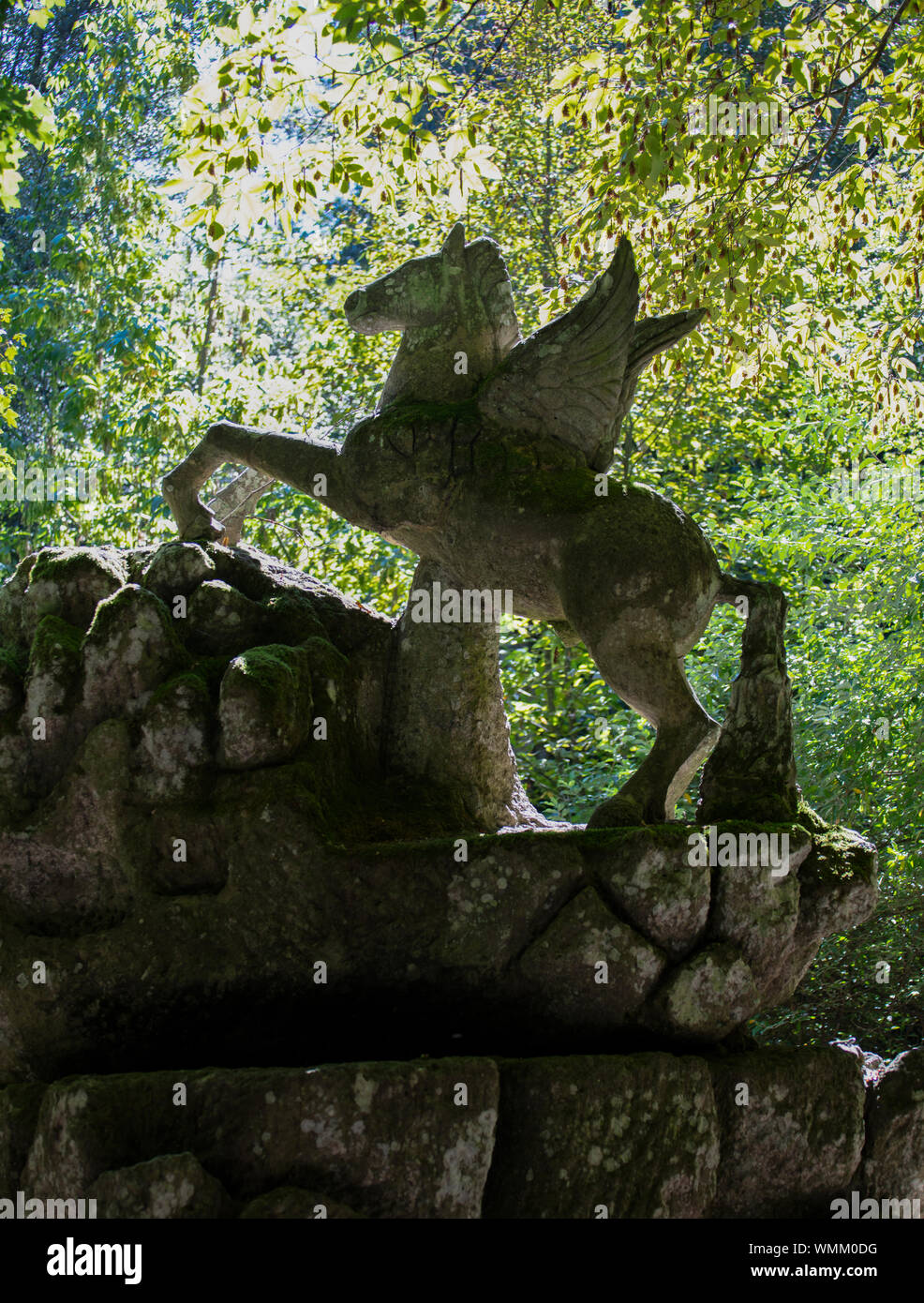 The giant statue of Pegasus in the gardens at Bomarzo, the Parco dei Mostri dating to the 16th century. The statue is backlit against green foliage. Stock Photo