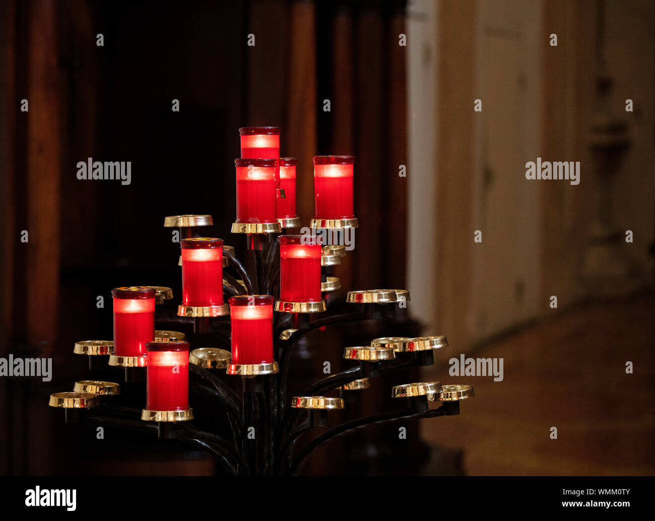 Red candles on a pyramid stand inside a building. Some of the candleholders are empty and some have lit candles in them. Stock Photo