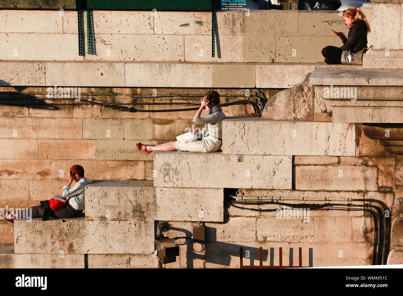 Authentic travel impressions from Paris: Sun bathers on the stairs of the Seine embankments Stock Photo