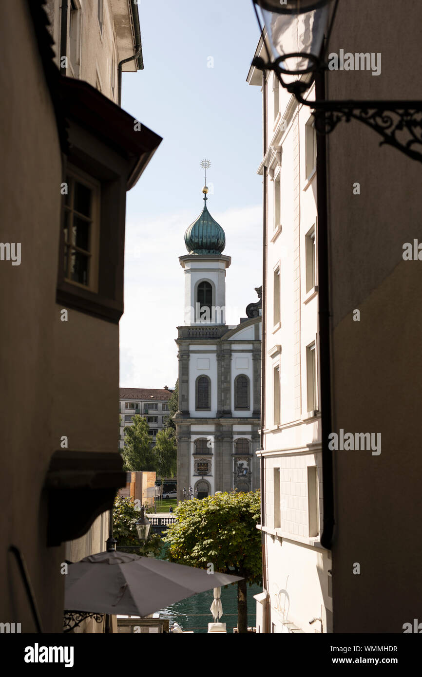 Peeking between buildings at one of the spires of the baroque Jesuit church in Lucerne, Switzerland. Stock Photo