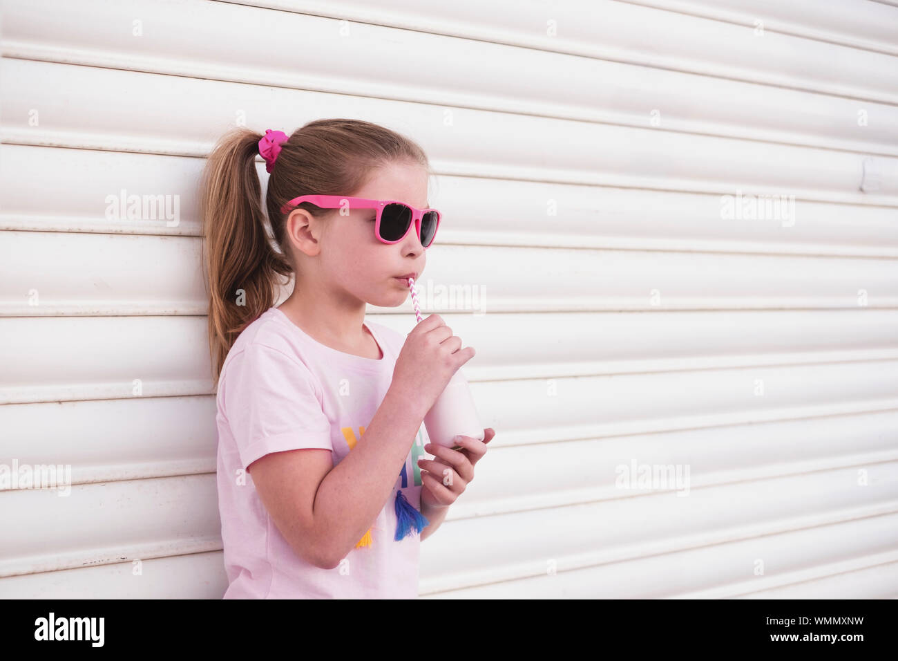 Young girl wearing pink sunglasses drinking milk through a straw Stock Photo