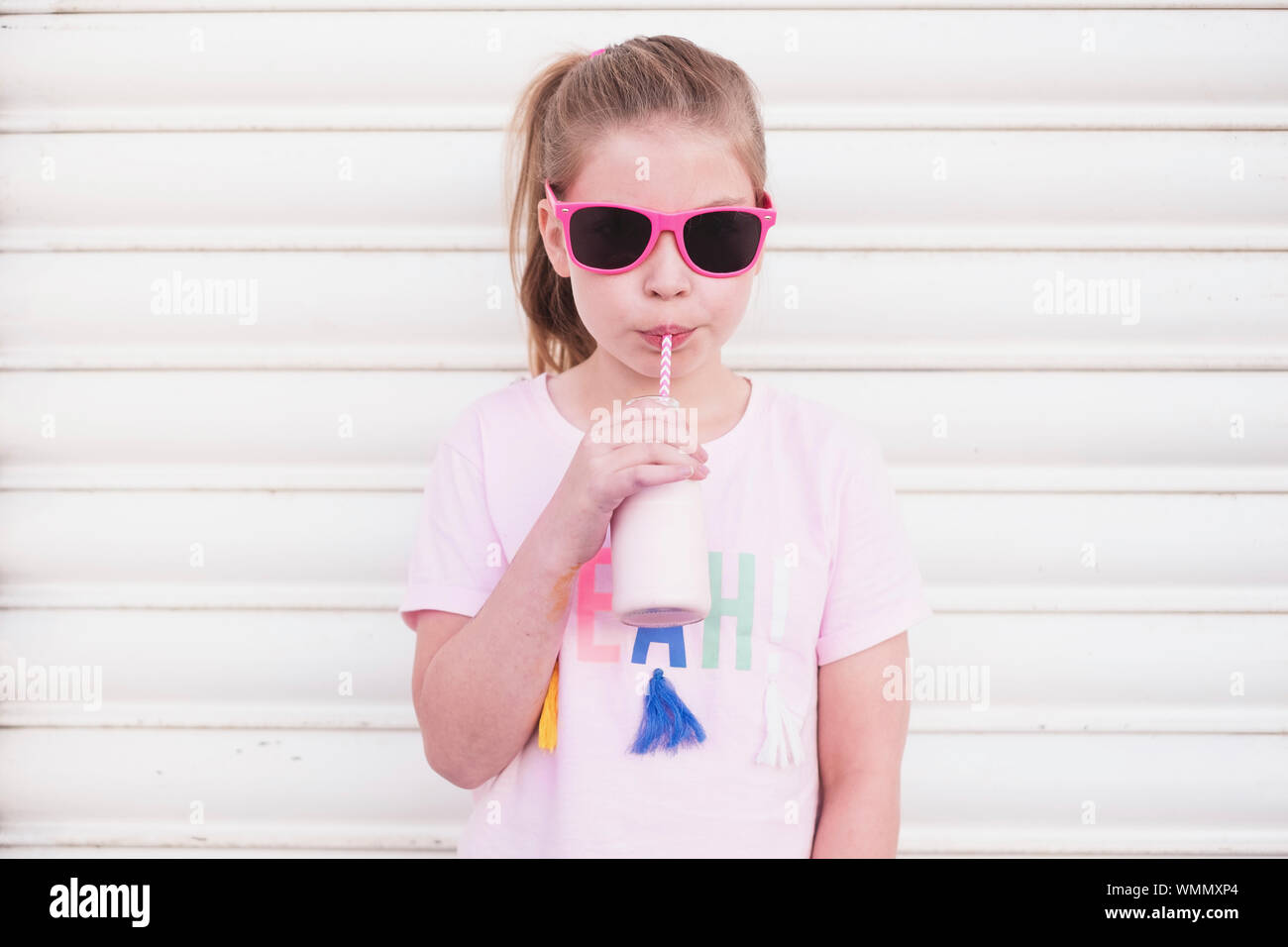 Young girl wearing pink sunglasses drinking pink milk through a straw Stock Photo