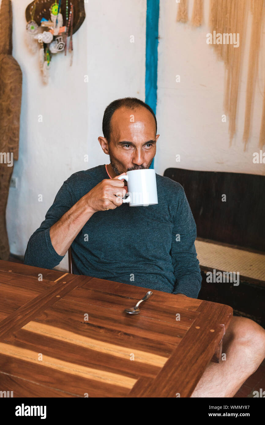 Mid aged hispanic male looking away and drinking a cup of coffe Stock Photo