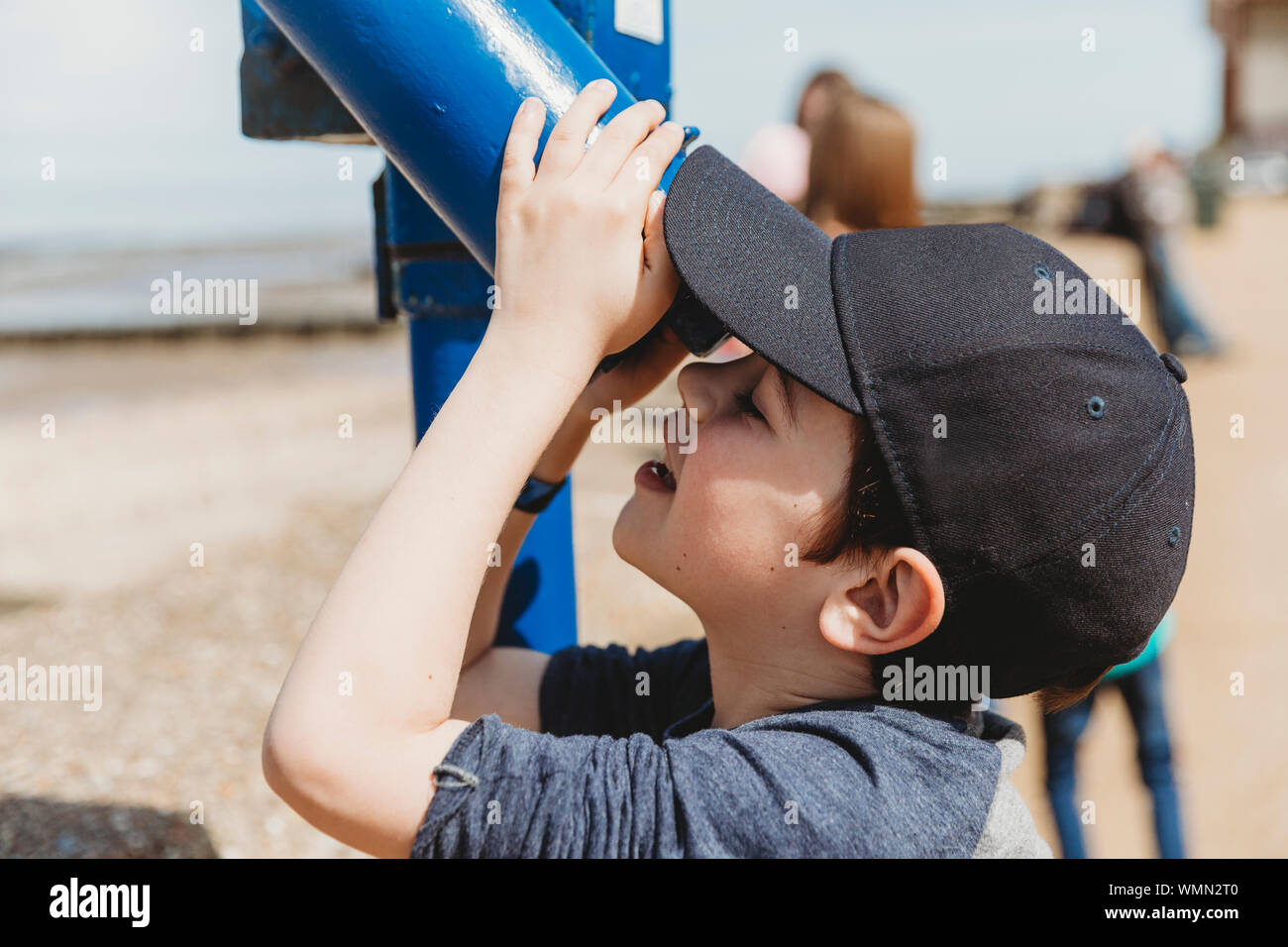 Boy wearing cap looking through telescope at  beach Stock Photo