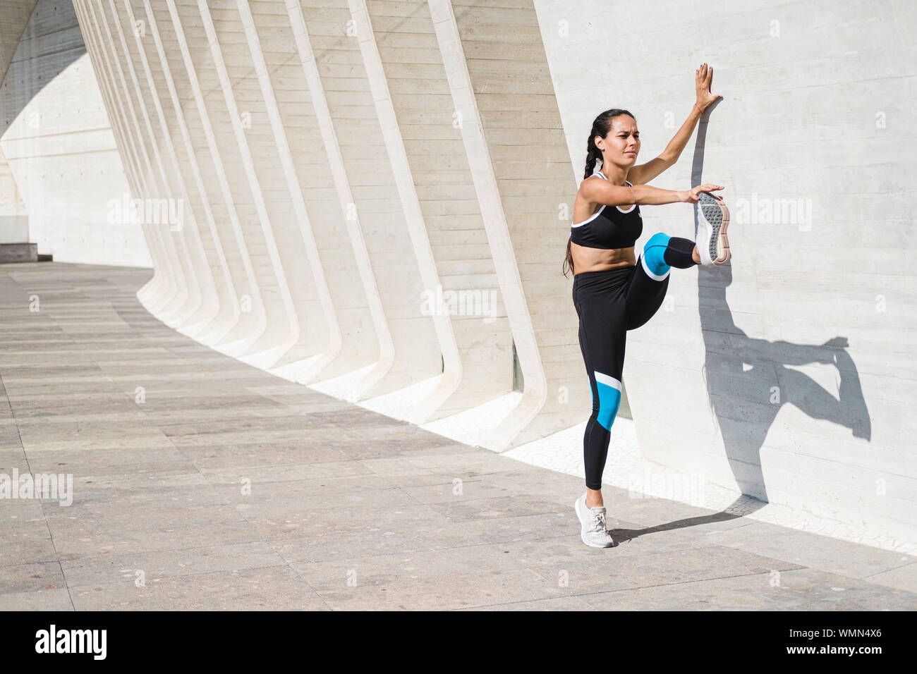 Full body of female athlete stretching legs against concrete wall Stock Photo