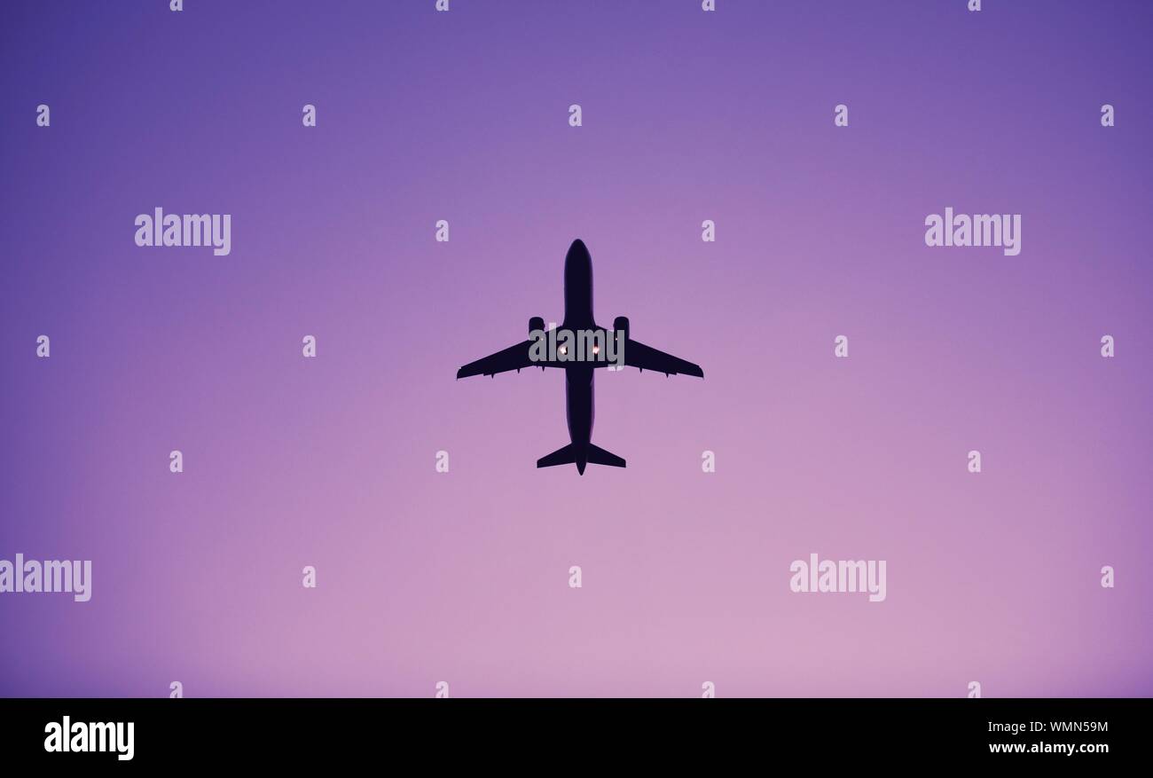 Directly Below Shot Of Silhouette Airplane Flying In Clear Purple Sky Stock Photo