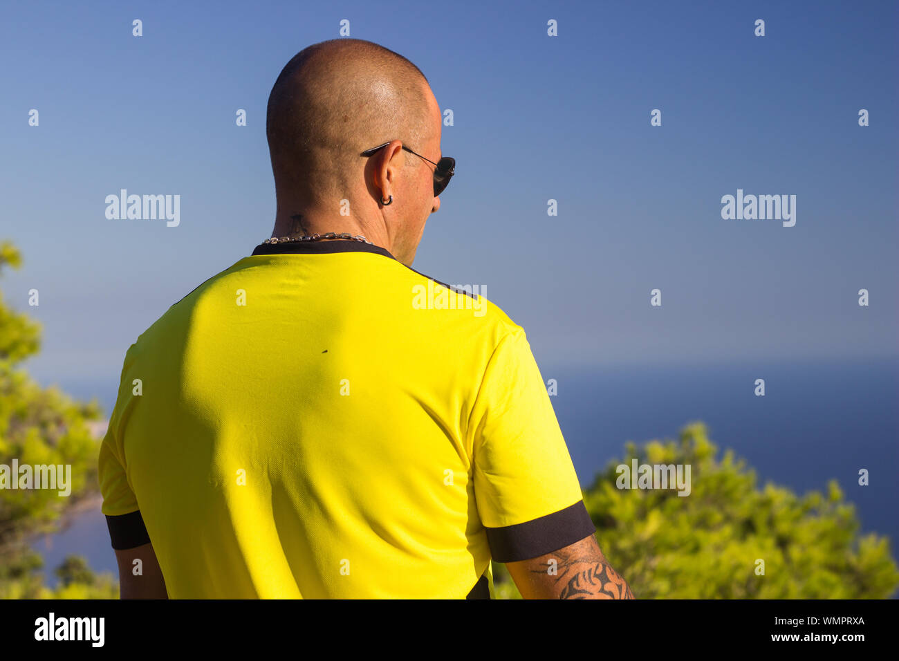 Man wearing yellow sport t shirt watching seascape, from behind Stock Photo