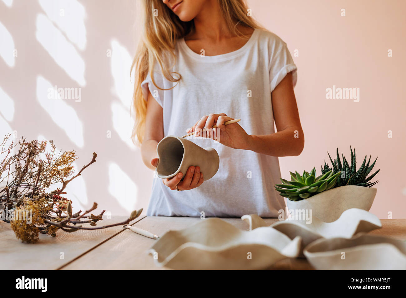 Young ceramic artist working in her studio. Female potter finishing a clay mug. Stock Photo