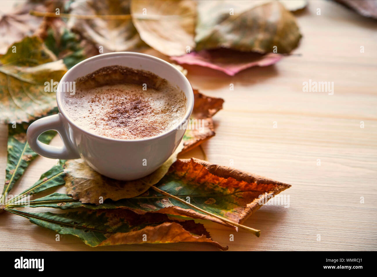 Autumn coffee cup with dried leaves decoration on wooden table, cozy fall deco concept, home lifestyle warm coffee cup in autumn season Stock Photo