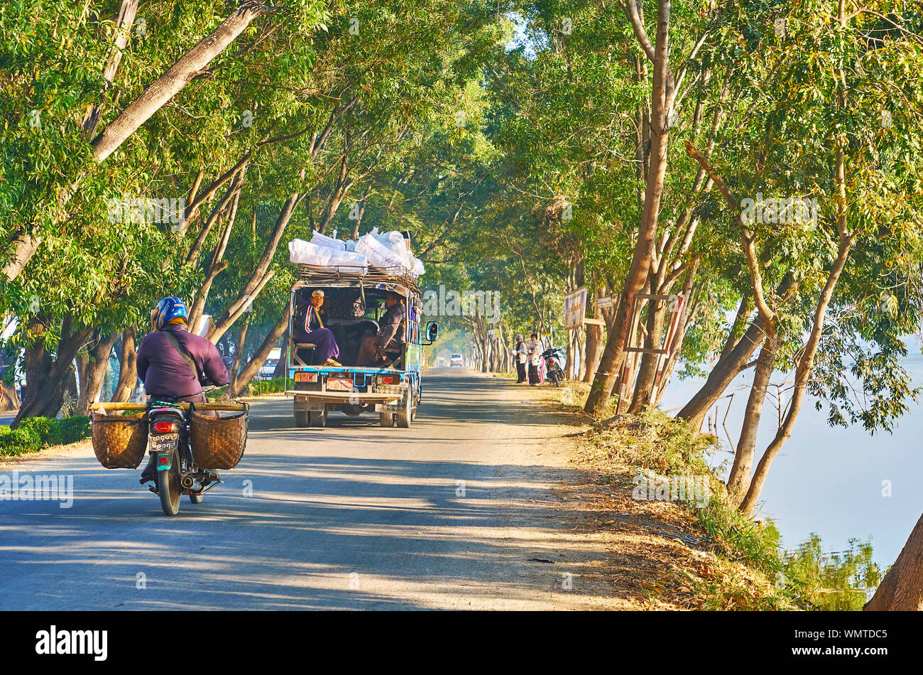 NYAUNGSHWE, MYANMAR - FEBRUARY 20, 2018: The traffic along the intercity road with green trees on both sides, the old truck rides with villagers in it Stock Photo