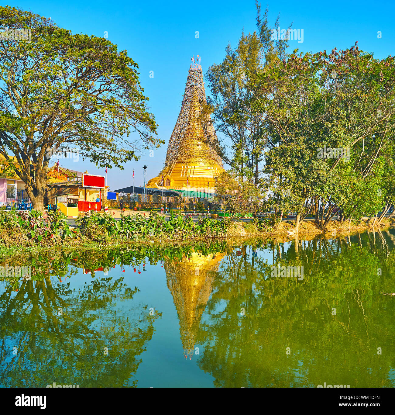 The spread green trees and golden Shwe Baww Di Pagoda are reflected on mirror surface of Tharzi Pond, Nyaungshwe, Myanmar Stock Photo
