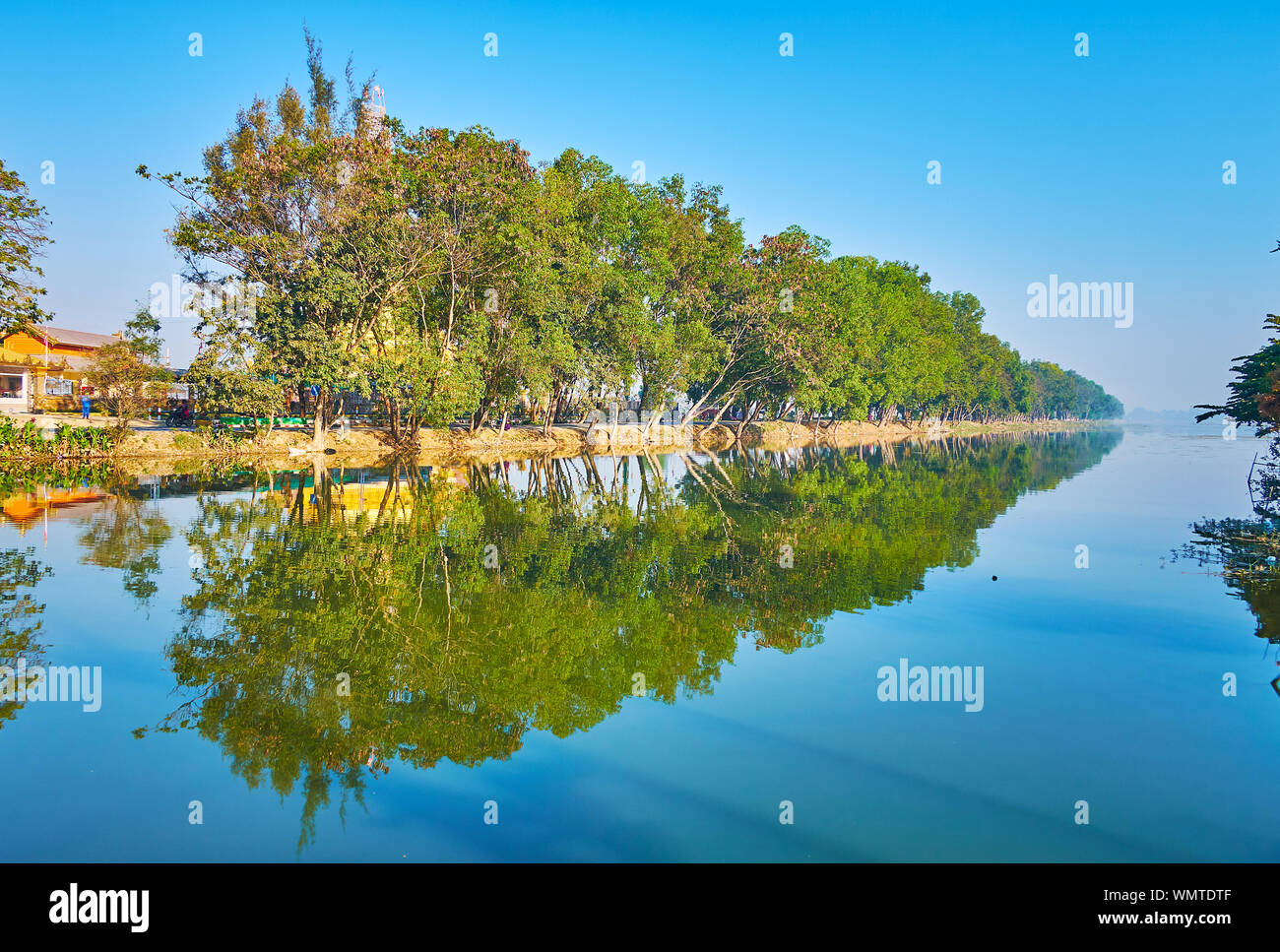 Tharzi pond boasts clear calm waters, reflecting line of tall shady trees, stretching along the banks, Nyaungshwe, Myanmar Stock Photo