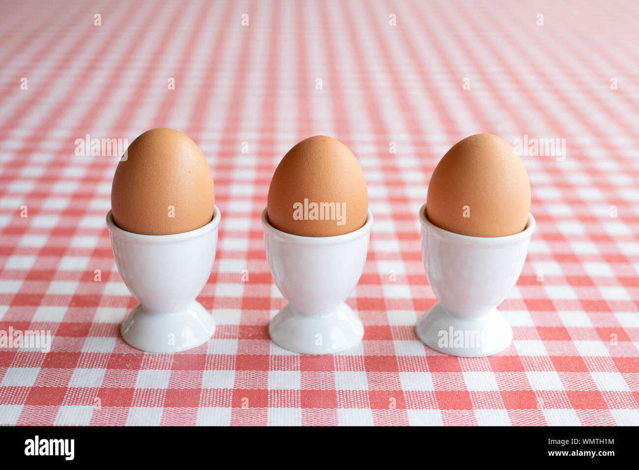 Three boiled eggs in egg cups in a row on a table Stock Photo