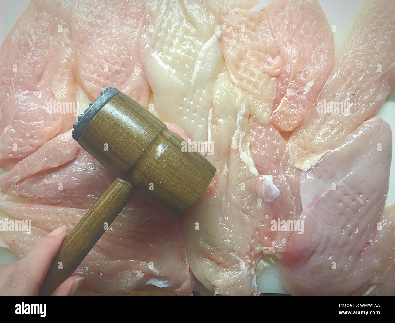 Cropped Hand Holding Tenderizer On Raw Chicken Meat Stock Photo