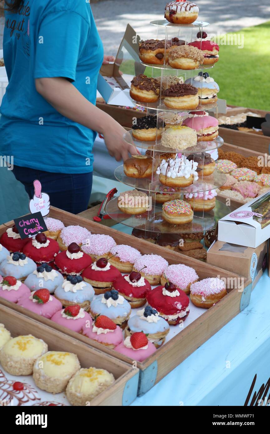 Calorific sugary tempting doughnut treats for sale at a food market some in trays and some on a cake stand Stock Photo